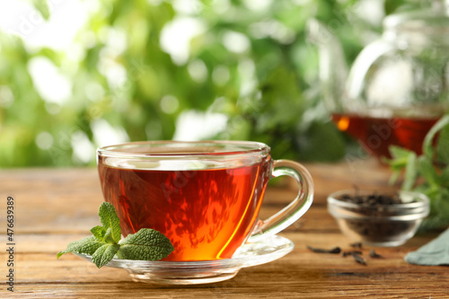Glass cup of aromatic black tea with fresh mint on wooden table against blurred background. Space for text