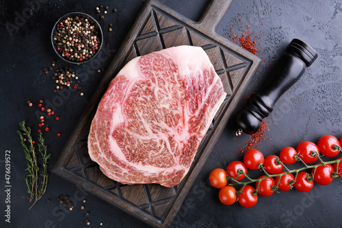 Raw meat. Japanese marble beef. Wagyu. Rib eye steak on a black wooden board on a black table with spices, thyme, cherry tomatoes. Background image, copy space, flatlay, top view