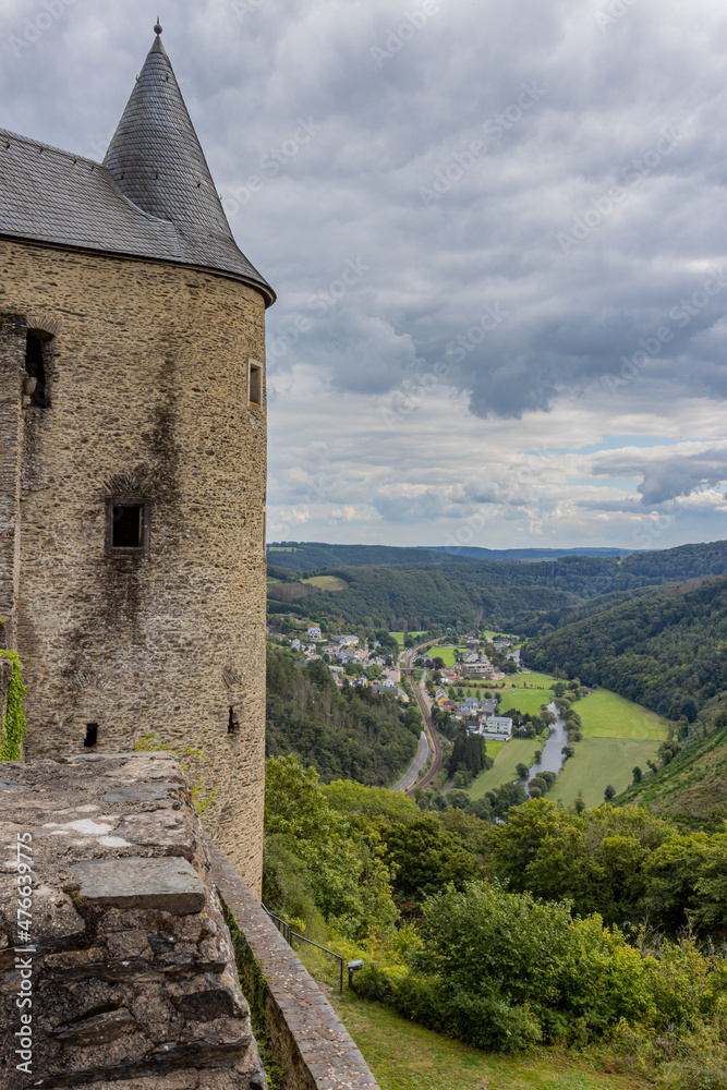 Castle tower, countryside landscape with hills covered with lush green trees, town of de Bourscheid, country road and its river in the background, cloudy day with a sky with gray clouds, Luxembourg
