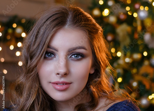 Young beautiful girl with loose hair close up sitting near the Christmas tree with Christmas toys