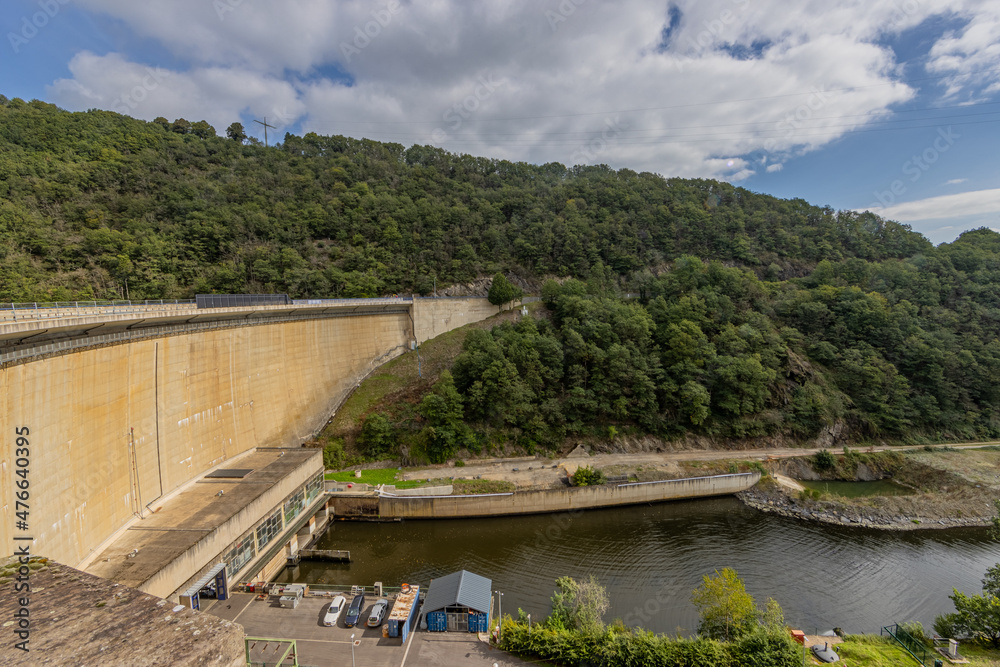 Top view of the Esch-sur-Sure dam, huge wall, hydroelectric complex, parking lot, hills with lush green trees and wild vegetation in the background, cloudy day with abundant clouds in Luxembourg