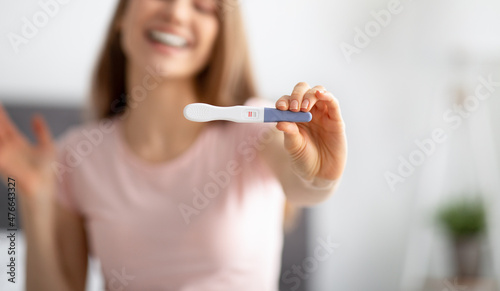 Closeup of young woman showing positive pregnancy test at camera  feeling happy to have baby at home  selective focus