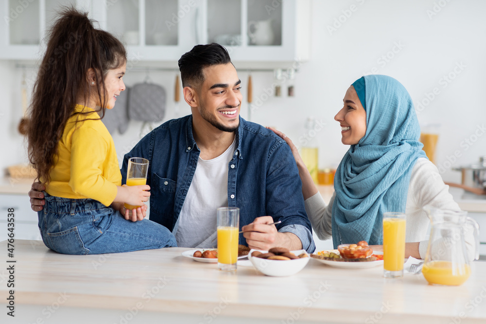 Cheerful Muslim family Of Three Having Breakfast In Kitchen, Chatting And Laughing