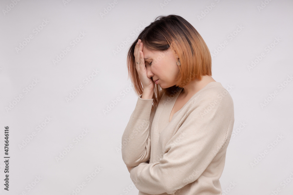 The upset girl covered her face with her hand while standing on a white background