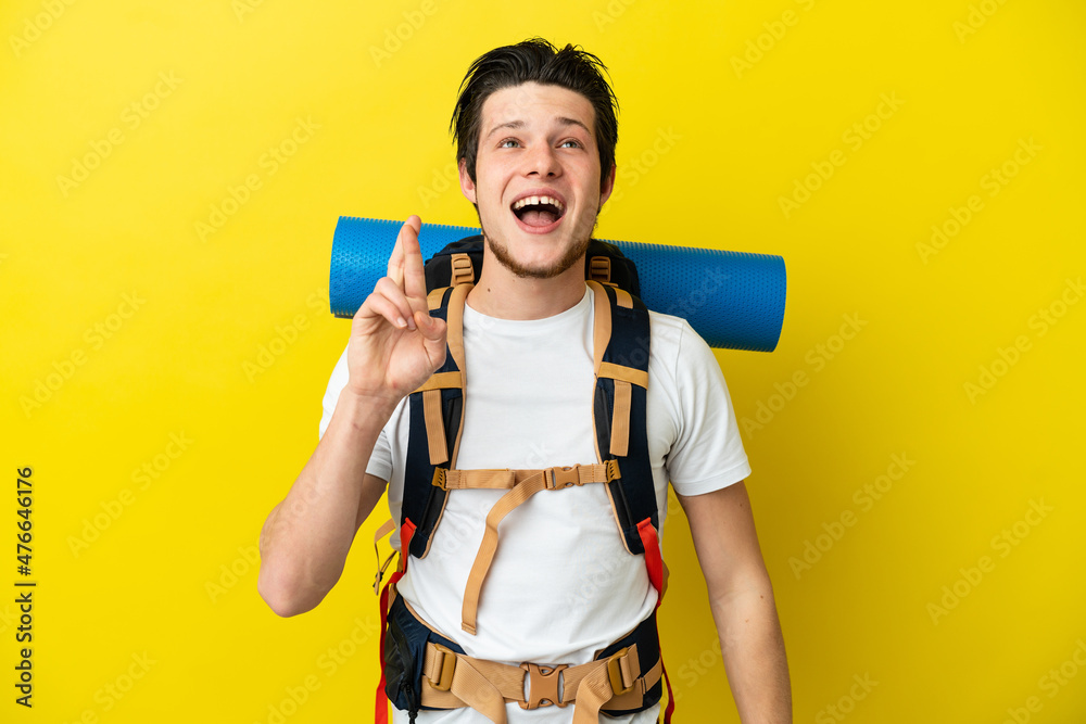 Young mountaineer Russian man with a big backpack isolated on yellow background with fingers crossing and wishing the best Young mountaineer Russian man with a big backpack isolated on yellow background with fingers crossing and wishing the best