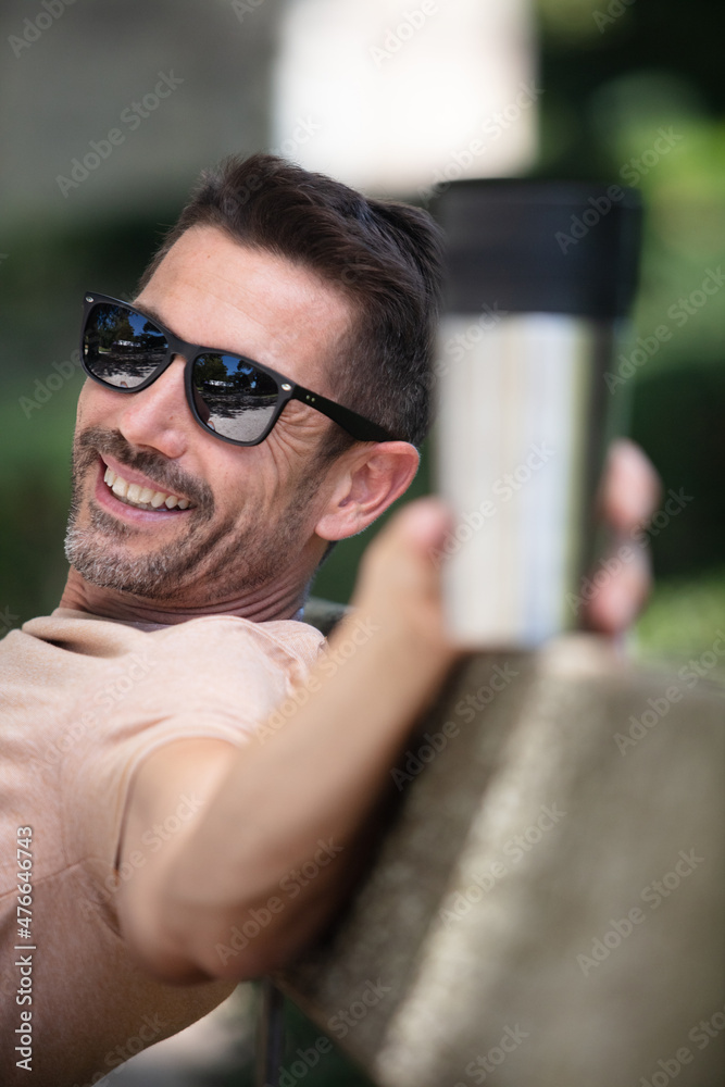 man sat on park banch holding an insulated drinking cup man sat on park banch holding an insulated drinking cup