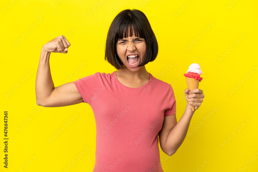 Pregnant woman holding a cornet ice cream isolated on yellow background doing strong gesture Pregnant woman holding a cornet ice cream isolated on yellow background doing strong gesture