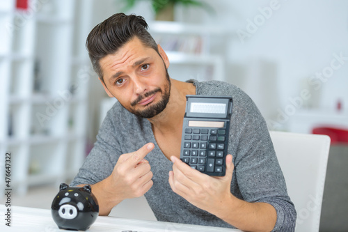 man with regretful expression holding pocket calculator and piggybank photo