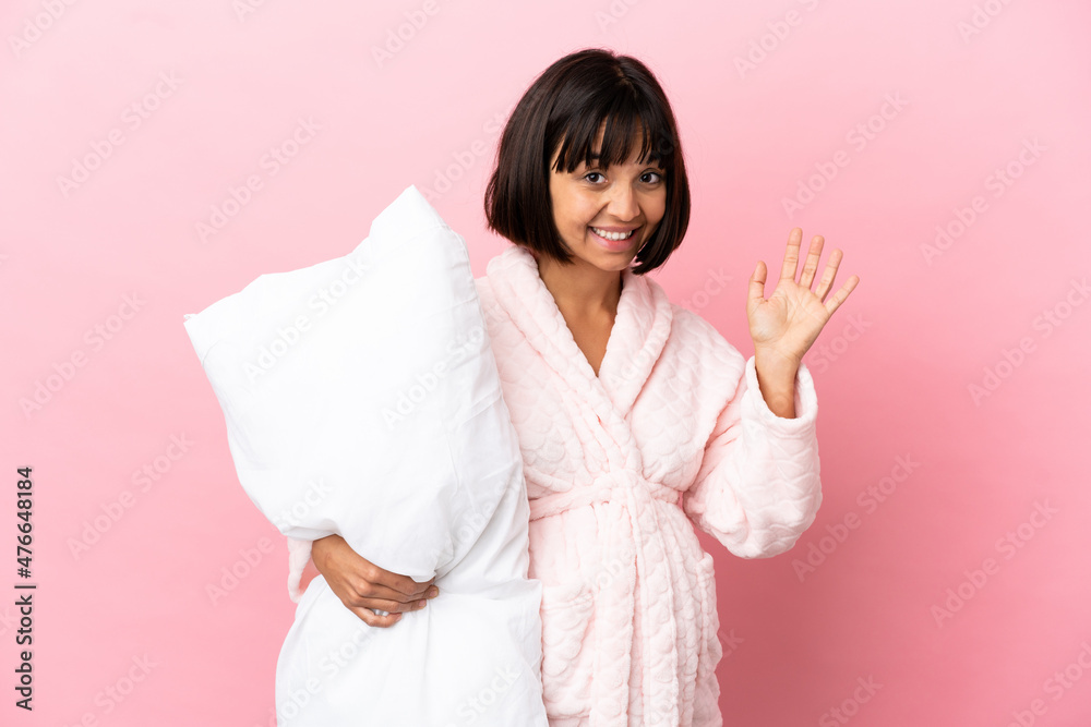 Pregnant woman in pajamas isolated on pink background saluting with hand with happy expression