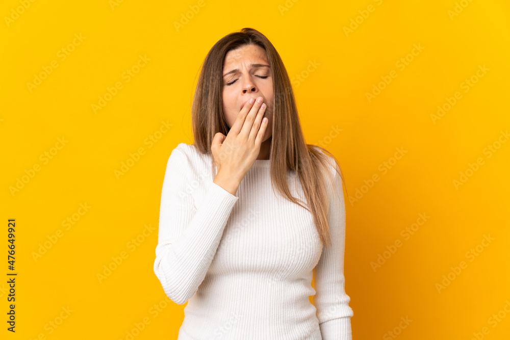 Young Slovak woman isolated on yellow background yawning and covering wide open mouth with hand