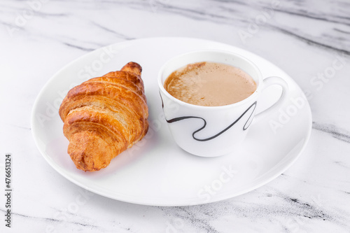 White ceramic plate with Cup of coffee and croissant on marble texture background.