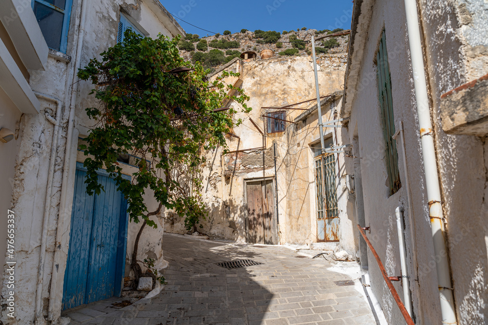 Eine kleine verwinkelte Gasse in einem Bergdorf auf Kreta, Griechenland mit altertümlichen Häusern und einer blauen Tür (Querformat)