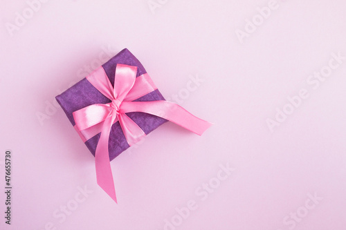 Top view of purple gift box with tied pink bow on the pink background. Copy space.