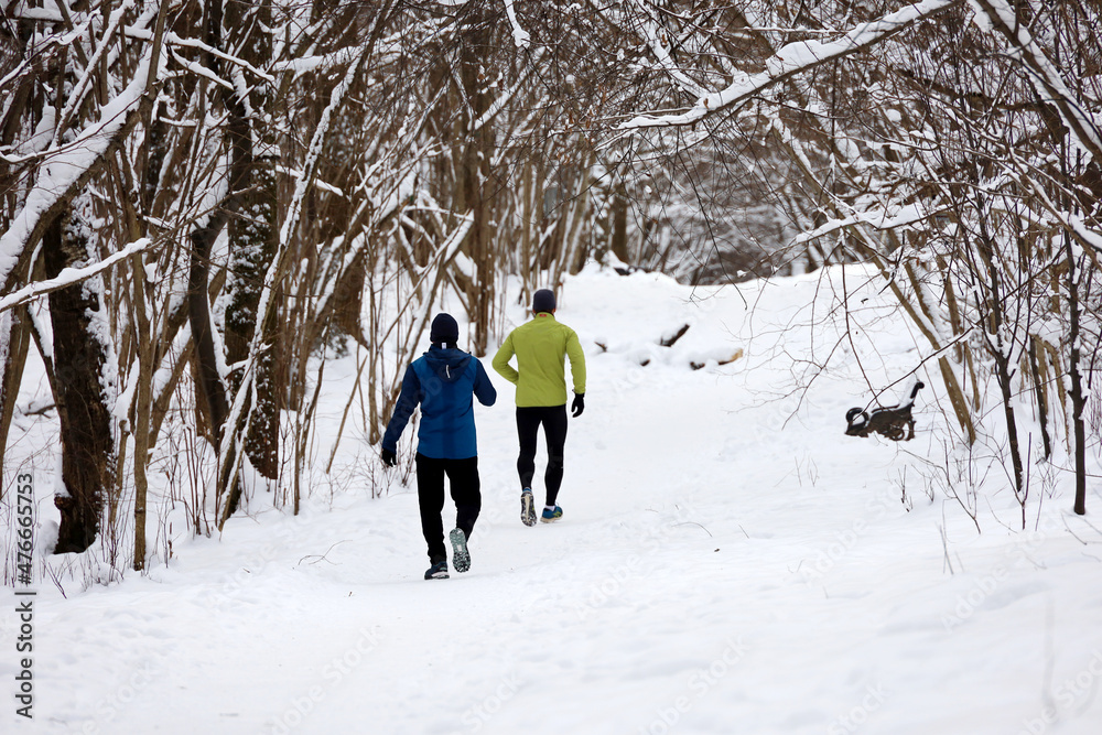 Two guys running in winter park by the snow. Workout, runners in cold season