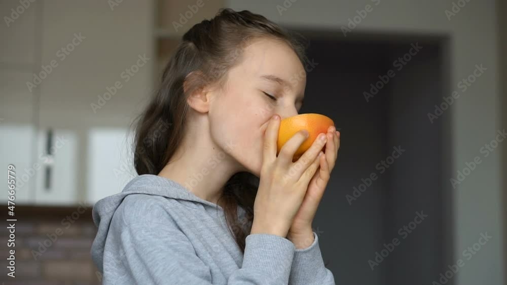 Little girl with long hair is licking a half of the orange. Happy childhood, healthy eating Little girl with long hair is licking a half of the orange. Happy childhood, healthy eating