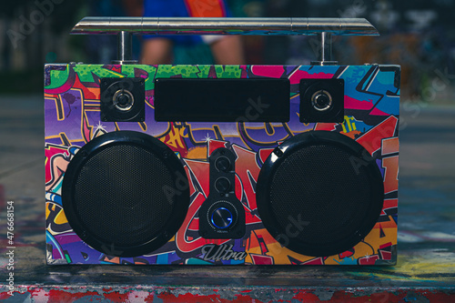 a colorfully decorated electronic boom box sits on the pavement of an outdoor skate park