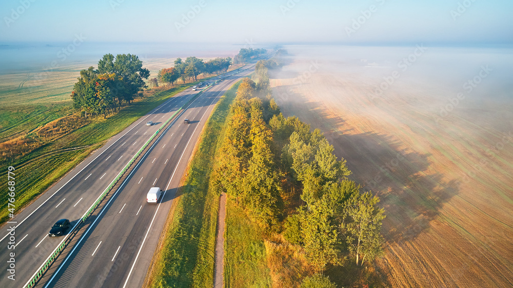 Sunny Magical autumn foggy morning. Aerial view of highway with cars. Asphalt road covered in fog. Early misty dawn.