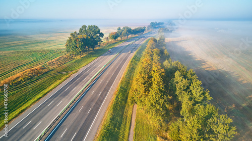 Aerial view of highway with cars. Asphalt road covered in fog. Early misty dawn.