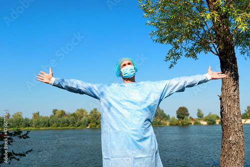 COVID-19 coronavirus pandemic. Unity with nature, good mood, peace and relaxation during the Virus Covid 19 crisis. Male doctor enjoying intense contact with nature. Open arms on the river bank. 