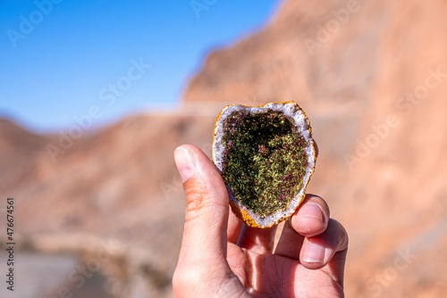 Closeup of person hand holding green amethyst geode on sunny summer day, Person showing cracked geode photo