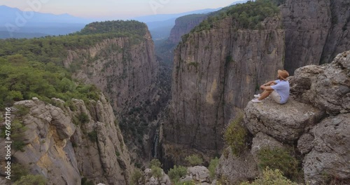 Tourist man sitting on the edge of the mountaing cliff against the backdrop of a gorge. Amazing Tazi Canyon ,Bilgelik Vadisi in Manavgat, Antalya, Turkey. Greyhound Canyon, Wisdom Valley. photo