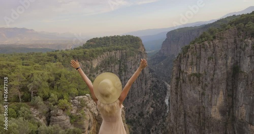 Tourist woman in white dress and hat standing with raised hands on the edge of a cliff against the backdrop of a gorge. Amazing Tazi Canyon ,Bilgelik Vadisi in Manavgat, Antalya, Turkey. Greyhound photo