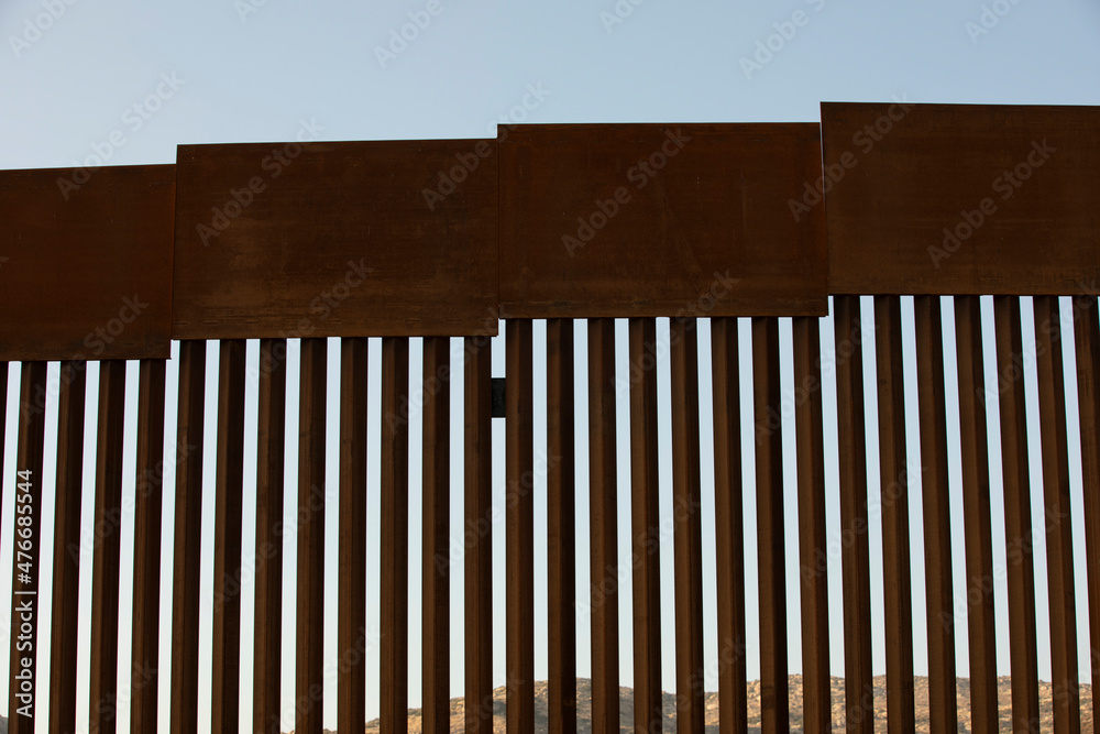 Tecate, Baja California, Mexico - September 14, 2021: Late afternoon sun shines on the USA Mexico border wall as it winds through Tecate. Tecate, Baja California, Mexico - September 14, 2021: Late afternoon sun shines on the USA Mexico border wall as it winds through Tecate.
