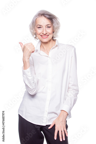 Portrait of a happy smiling mature woman in her sixties with trendy grey hair making thumbs up hand sign expressing approval isolated on white background