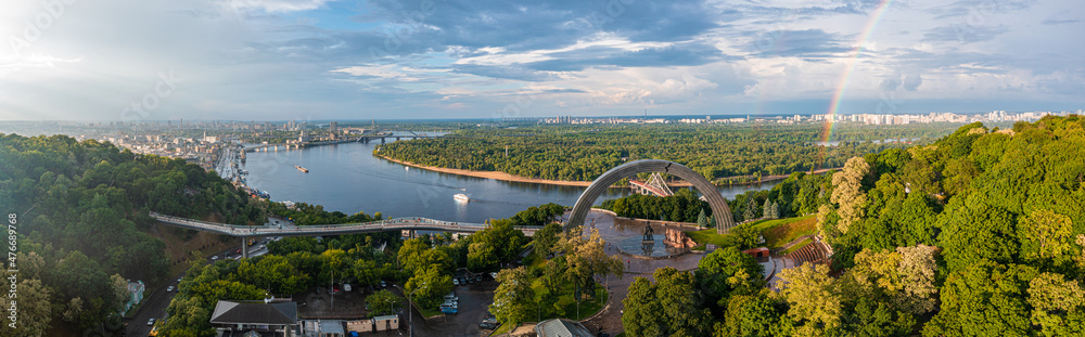 Fototapeta premium Panoramic view of Kyiv city with a beautiful rainbow over the city. Aerial view of the Arch of Friendship of Peoples.