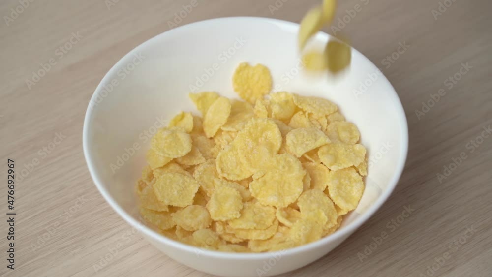 Close-up view slow motion of pouring golden healthy and hearty corn flakes into a white plate close-up view. Healthy breakfast preparation. Close-up view slow motion of pouring golden healthy and hearty corn flakes into a white plate close-up view. Healthy breakfast preparation.