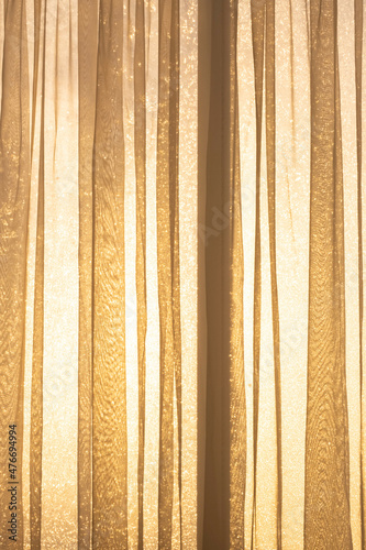 Rays of sun light shines through transparent curtain and frosty window from outdoor to room, close up.