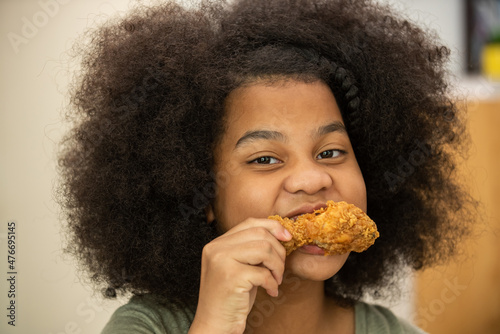 Close up of Little African girl biting delicious deep fried chicken with happiness. Happy family enjoy having dinner with eating and sharing a meal together at home.