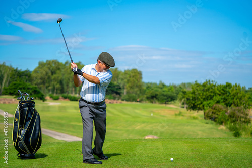 Asian senior man holding golf club hitting golf ball on fairway at country club in sunny day. Healthy elderly male golfer enjoy outdoor activity sport golfing at golf course on summer vacation