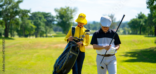 Asian man golfer walking on fairway together with female caddy on the green at golf course in sunny day. Healthy male enjoy outdoor lifestyle activity sport golfing at country club on summer vacation photo
