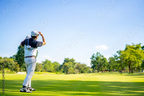 Confidence Asian man golfer holding golf club hitting golf ball on the green at golf course in sunny day. Healthy male enjoy outdoor lifestyle activity sport golfing at country club on summer vacation
