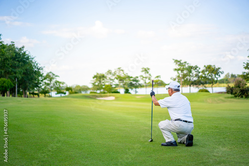 Asian senior man holding golf club hitting golf ball on fairway at country club in sunny day. Healthy elderly male golfer enjoy outdoor activity sport golfing at golf course on summer vacation
