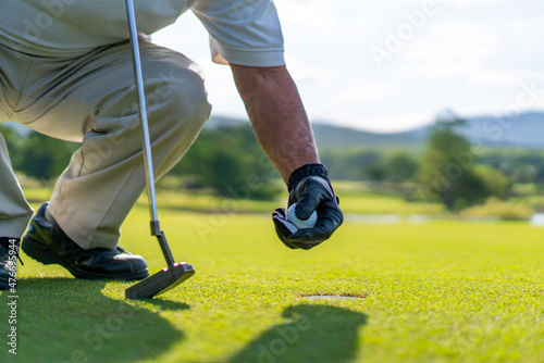 Close up hand of Asian senior man golfer picking golf ball out of the hole on green at golf course. Healthy male enjoy outdoor lifestyle activity sport golfing at country club on summer vacation