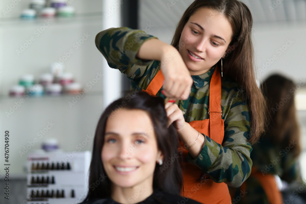 Smiling hairdresser creating fancy hairstyle for female client Smiling hairdresser creating fancy hairstyle for female client
