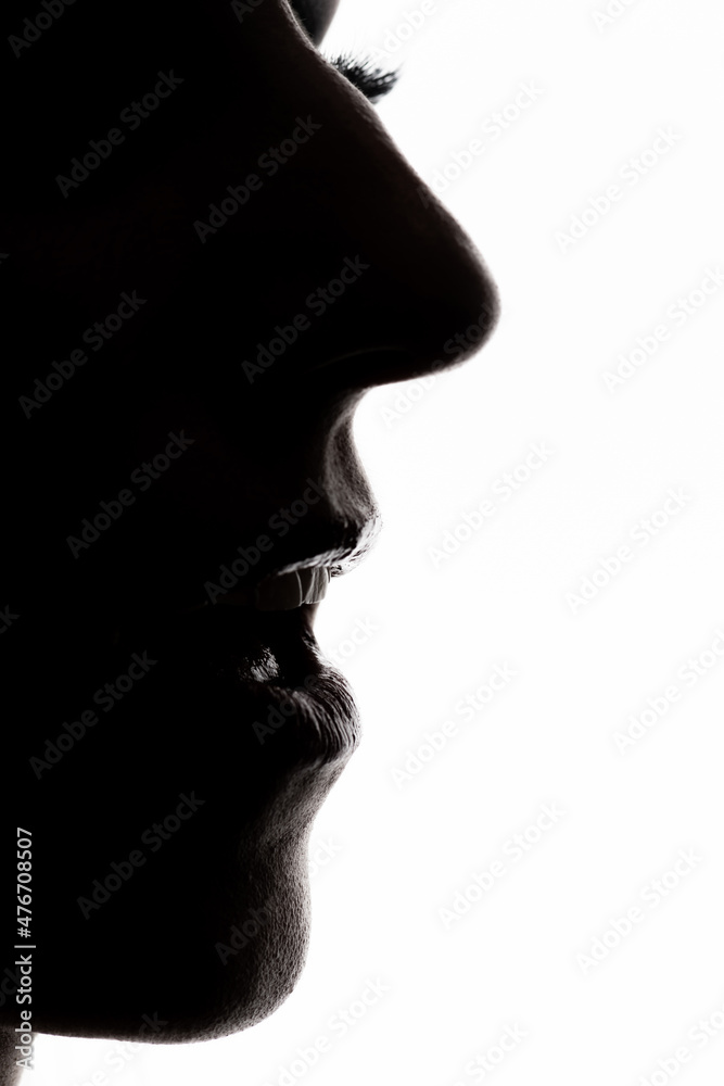 Womans face with a partially open mouth with visible teeth and eyebrows dark profile silhouette on a white glowing background with a copy space. Selective focus and image with shallow depth of field