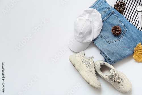 Stylish female shoes, cap, jeans, sweater, wristwatch and autumn decor on white background