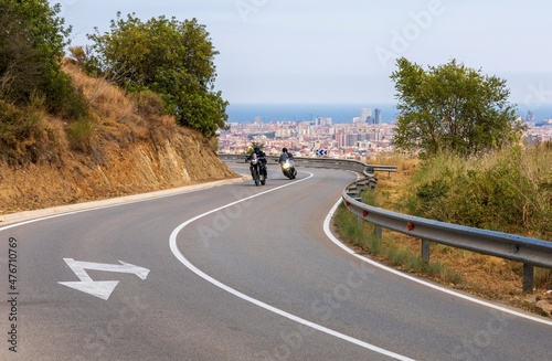 Motorcycles riding on a winding road with the city of Barcelona in the background
