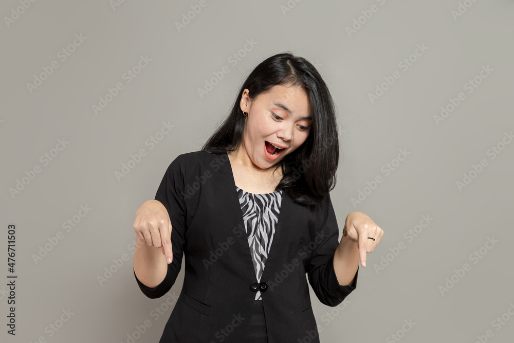 Young woman wearing a black suit is pointing and looking down with surprised expression with gaping mouth Young woman wearing a black suit is pointing and looking down with surprised expression with gaping mouth
