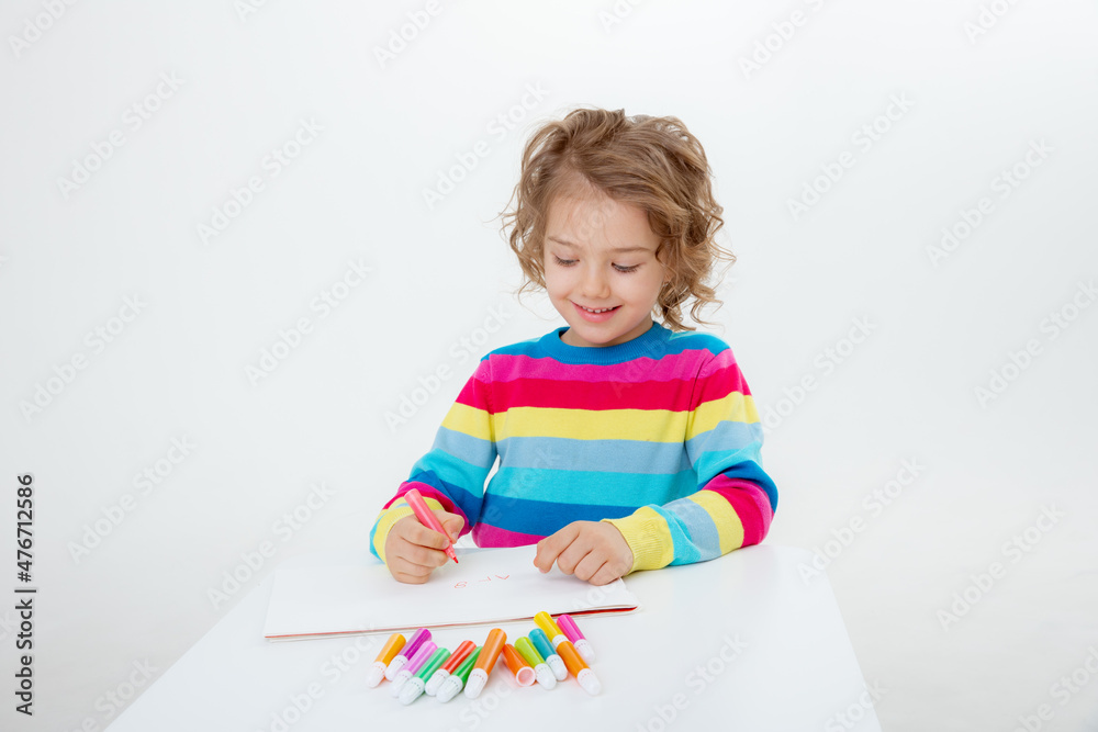 a little cute girl draws at the table with pencils isolated on a white background a little cute girl draws at the table with pencils isolated on a white background