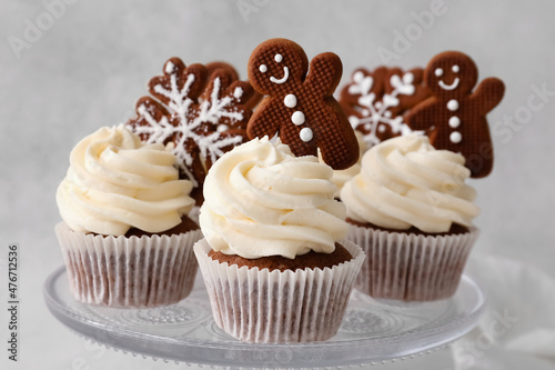 Stand of tasty Christmas cupcakes with gingerbread cookies on light background