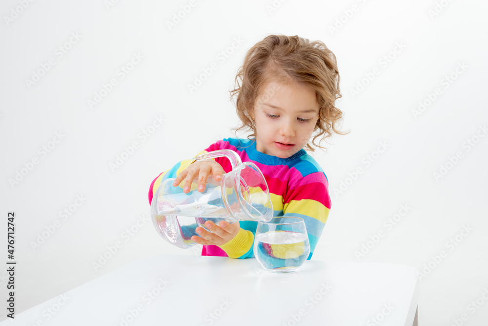 a little cute girl holds a jug of water, pours water into a glass isolated on a white background a little cute girl holds a jug of water, pours water into a glass isolated on a white background