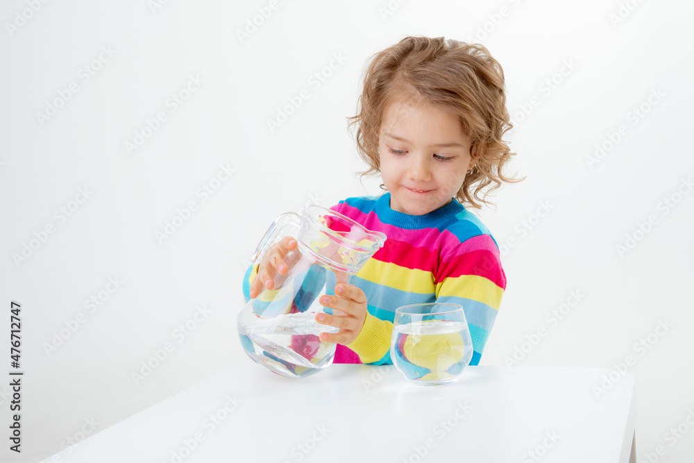 a little cute girl holds a jug of water, pours water into a glass isolated on a white background a little cute girl holds a jug of water, pours water into a glass isolated on a white background