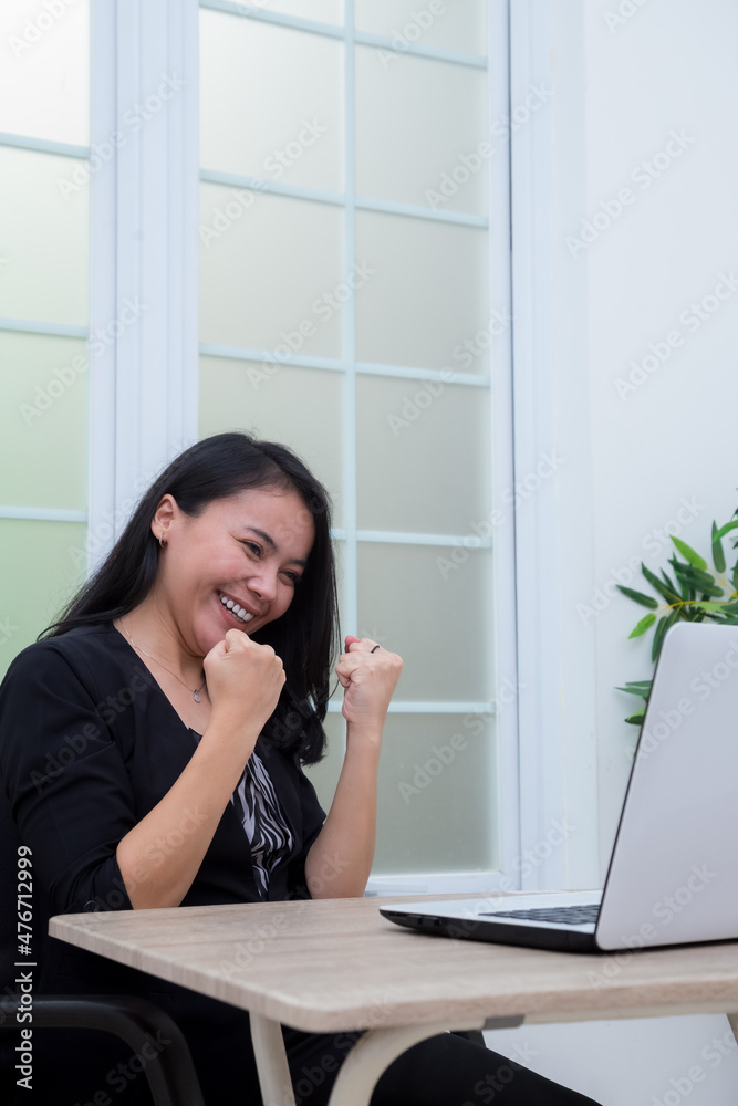 Business woman sitting on chair while raising both hands with success expression in front of laptop Business woman sitting on chair while raising both hands with success expression in front of laptop