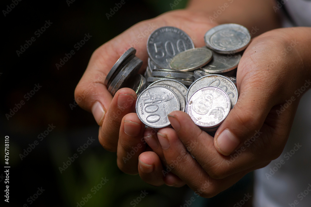 An Asian child holds Indonesian coin money, Rupiah, in shallow focus An Asian child holds Indonesian coin money, Rupiah, in shallow focus