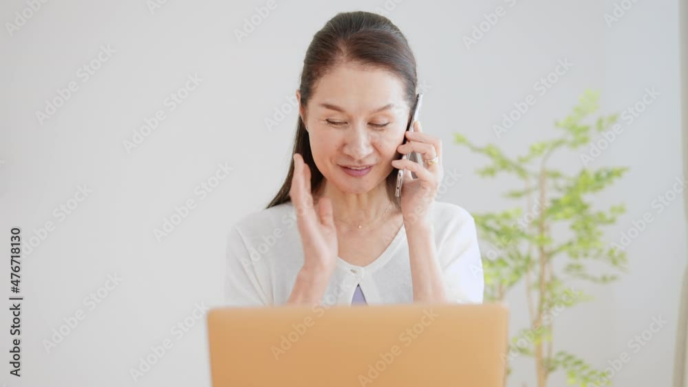 パソコンを見ながら電話をかけるシニア女性