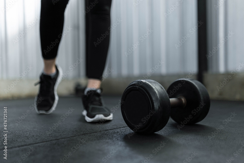 exercise concept The black rubber coated round dumbbell lying on the gym ground in front of the person who wears black trainers